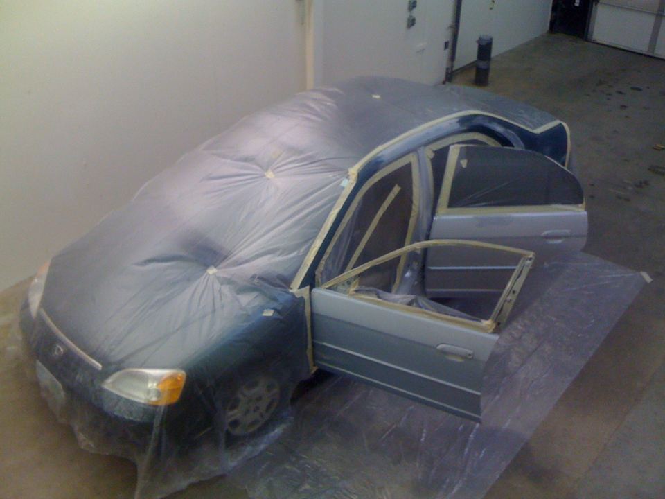 Honda Civic masked in the paint booth with a new door fitted