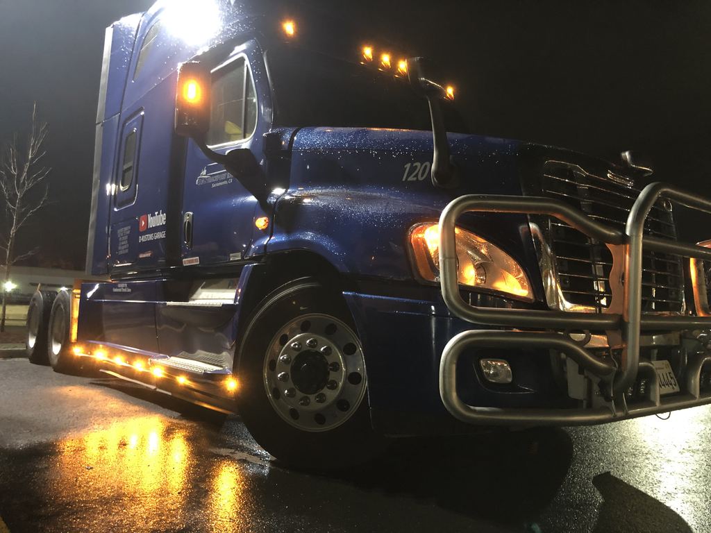 Blue semi-truck at night with amber LED lights along the side skirt, grille and visor