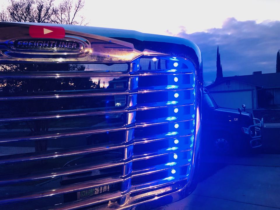 Close-up of a chrome semi-truck grille lined with blue LED lights
