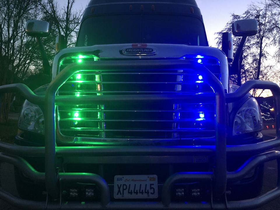 Semi-truck grille lit with green and blue LED lights at dusk